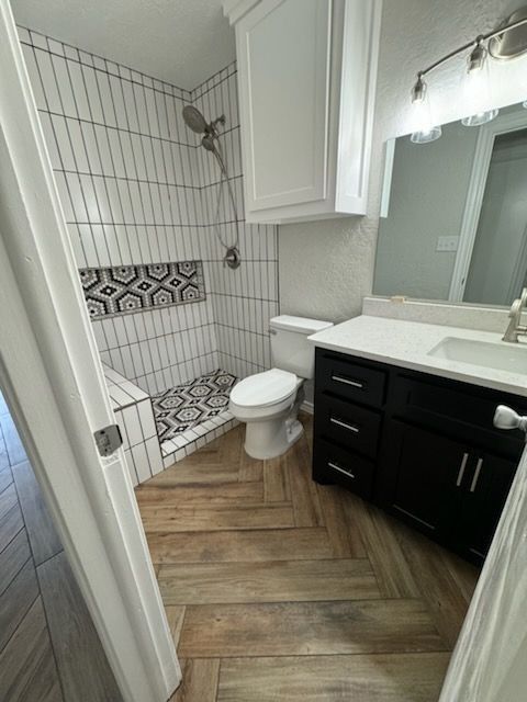 Bathroom with white and patterned tile shower, dark vanity, and wood-look floor.