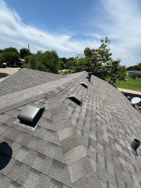 Gray shingle roof with several square vents, blue sky, and trees in the background.