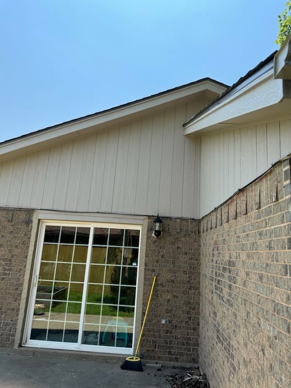 Exterior view of a building with a brick wall, sliding glass door, and cream-colored siding under a blue sky.
