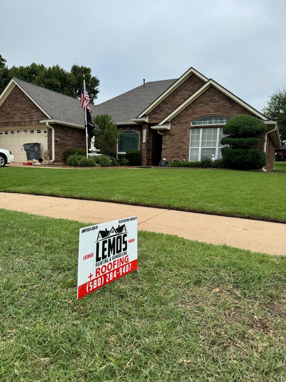 Sign in front of a brick house with the name of a roofing company.