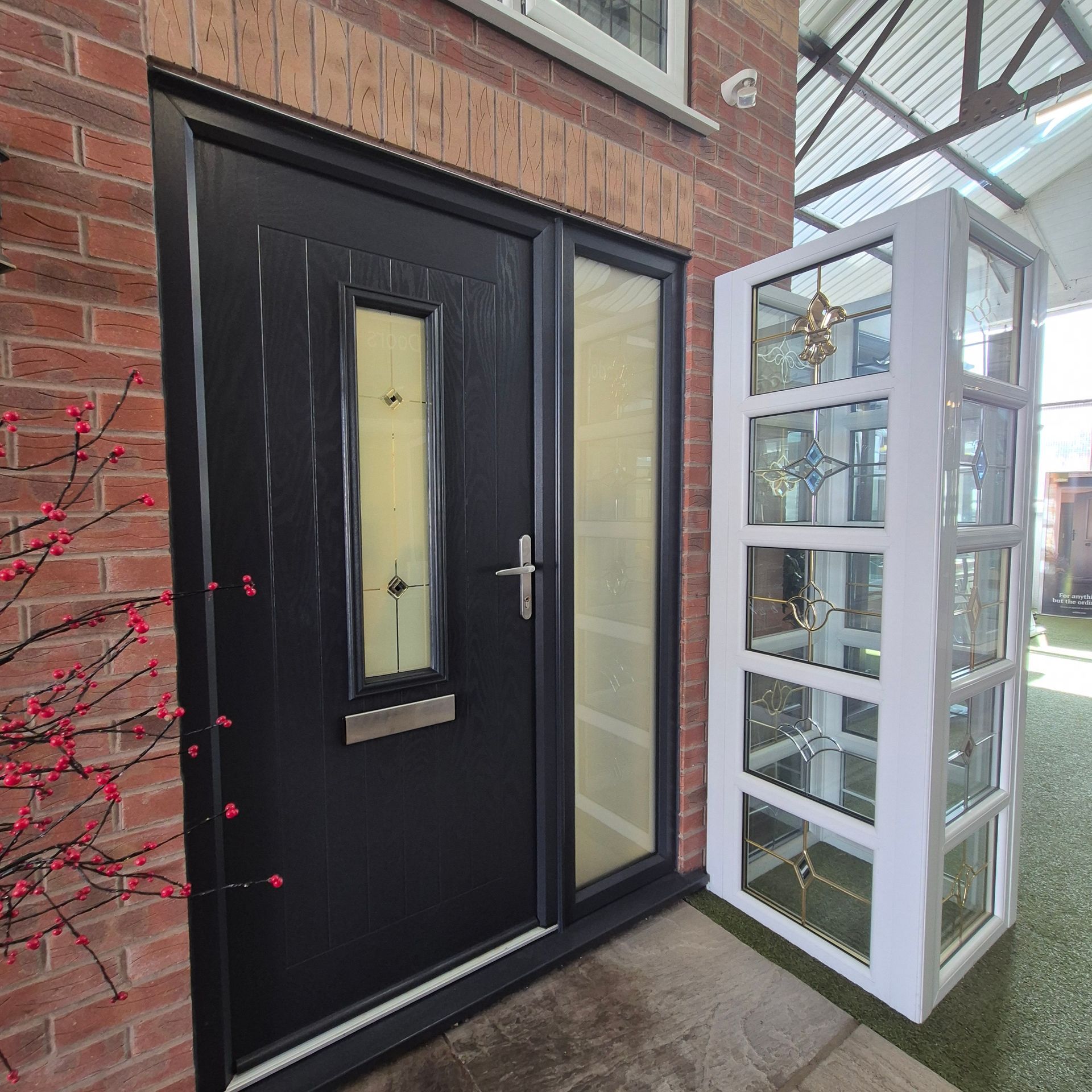 Black front door with sidelight next to a white decorative glass panel, in a brick facade setting.