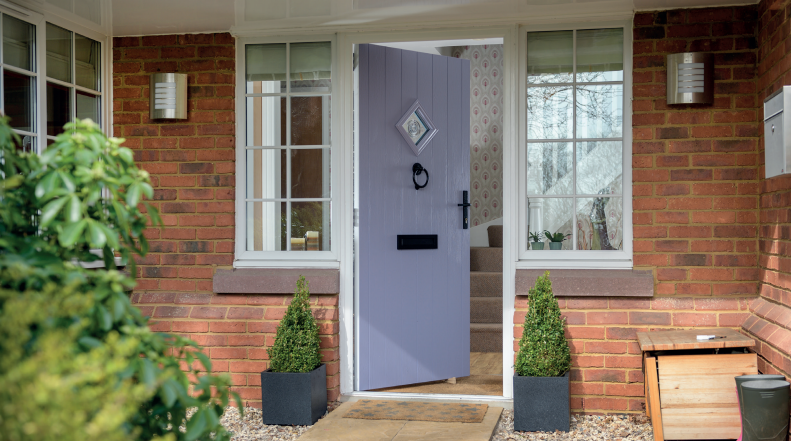 Purple front door ajar, flanked by windows. Red brick exterior with potted plants and mail box.