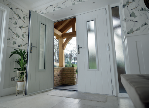 Double white doors with glass panels open to a porch with exposed wooden beams and a view of trees.