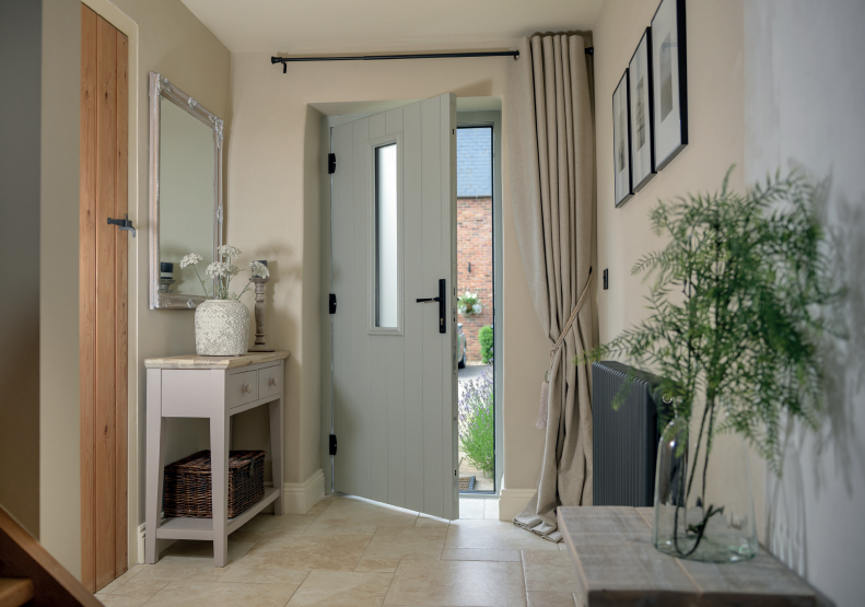 Hallway with open grey door, side table, mirror, and vase with greenery.