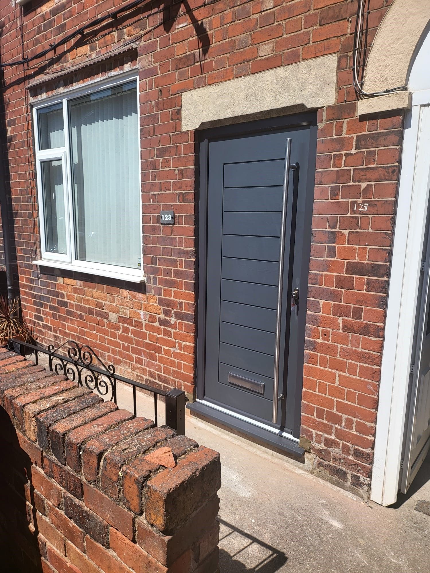 Gray front door on brick house with window and brick wall.