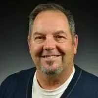 Smiling man with short gray hair and goatee against a dark background