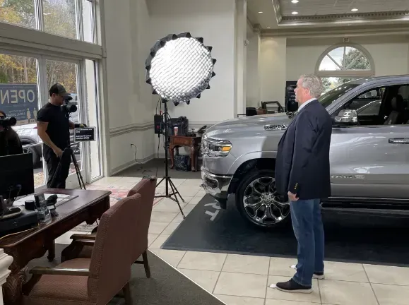 Photo shoot setup in a bright showroom with a silver SUV and a large studio light.