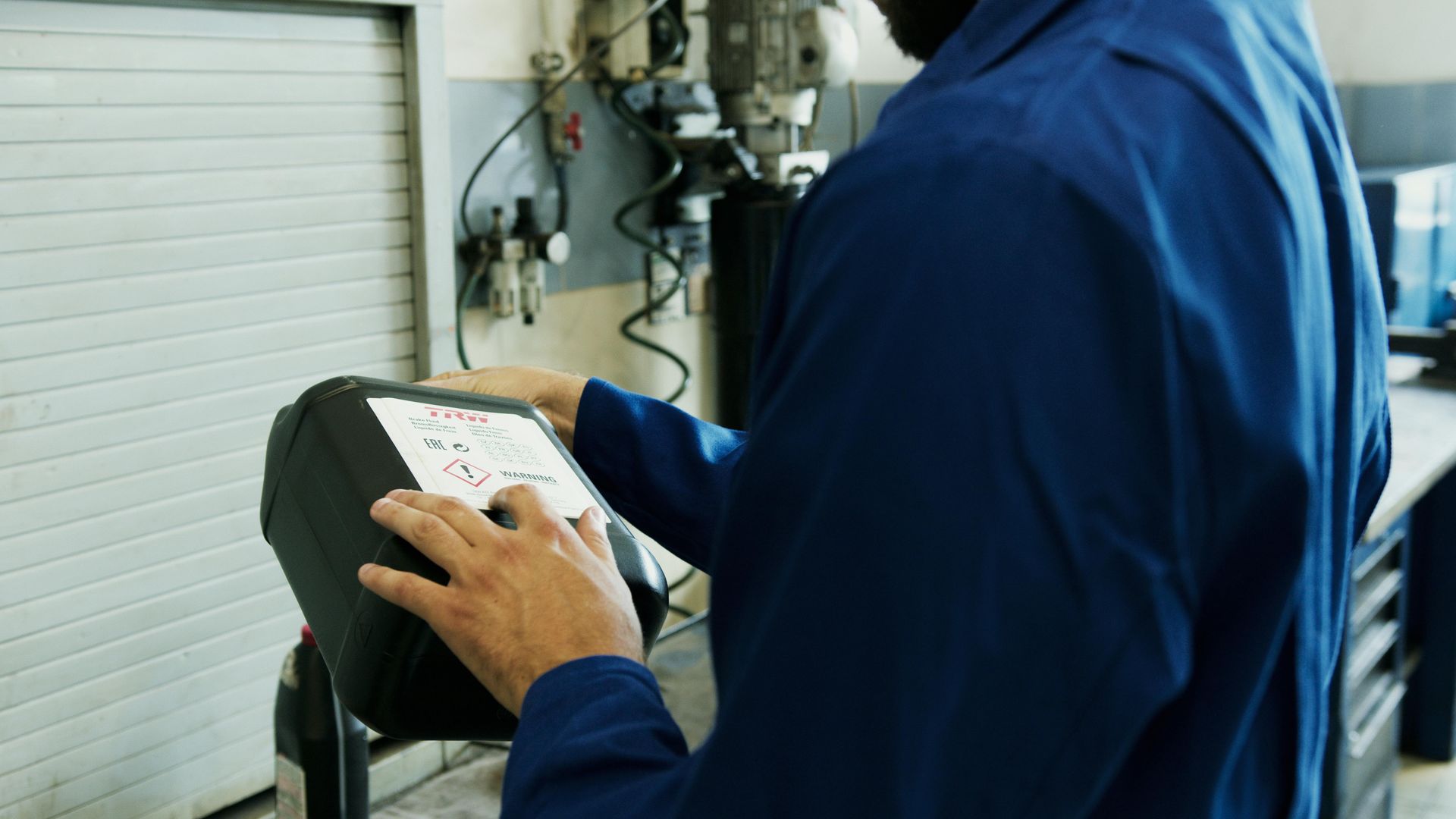 Kumeu Car Services mechanic in blue uniform operates a black machine in a workshop.