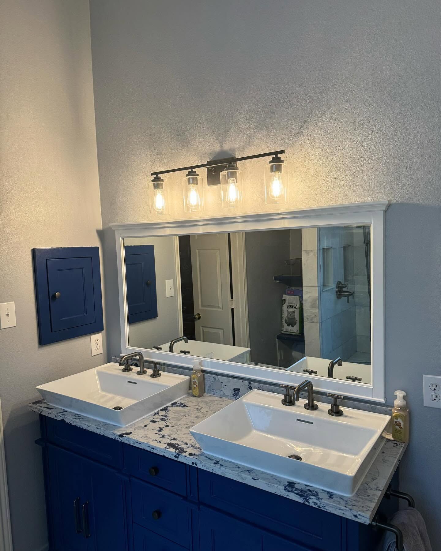 Modern bathroom vanity with double sinks, blue cabinets, large mirror, and wall light fixture