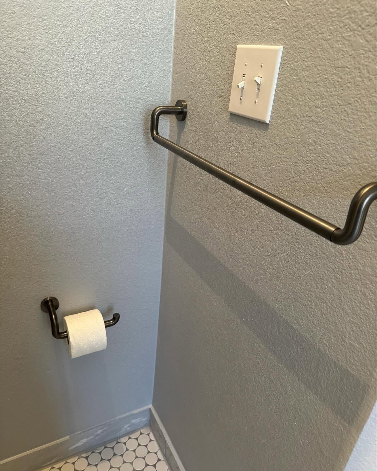 Bathroom grab bar beside a toilet paper holder on a gray textured wall.