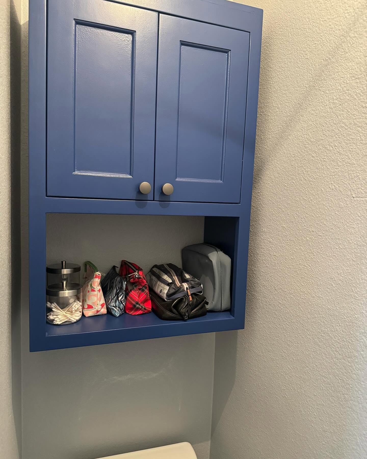 Blue wall cabinet with cabinet doors and toiletries stored on the shelf below