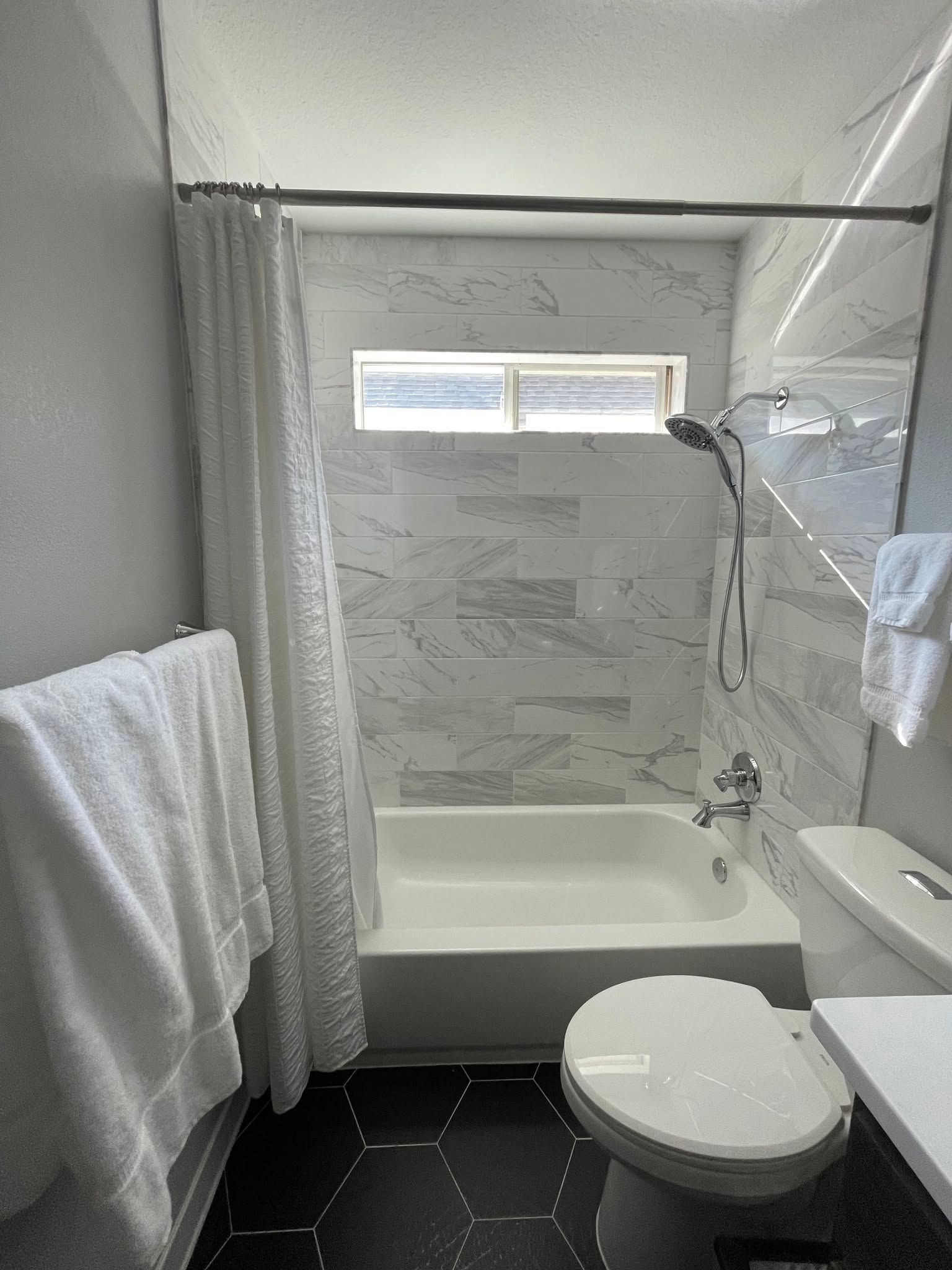 Small bathroom with a white tub, toilet, towel rack, and window above the shower.