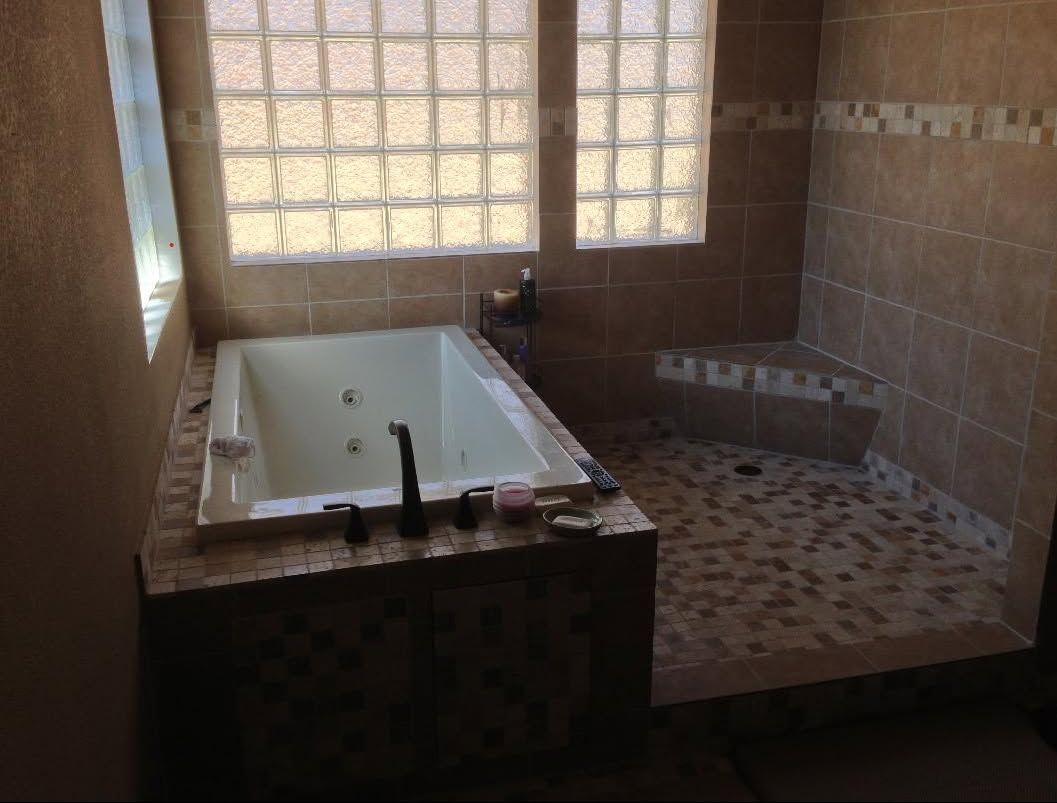 Bathroom with a white bathtub and tiled shower area lit by a window.