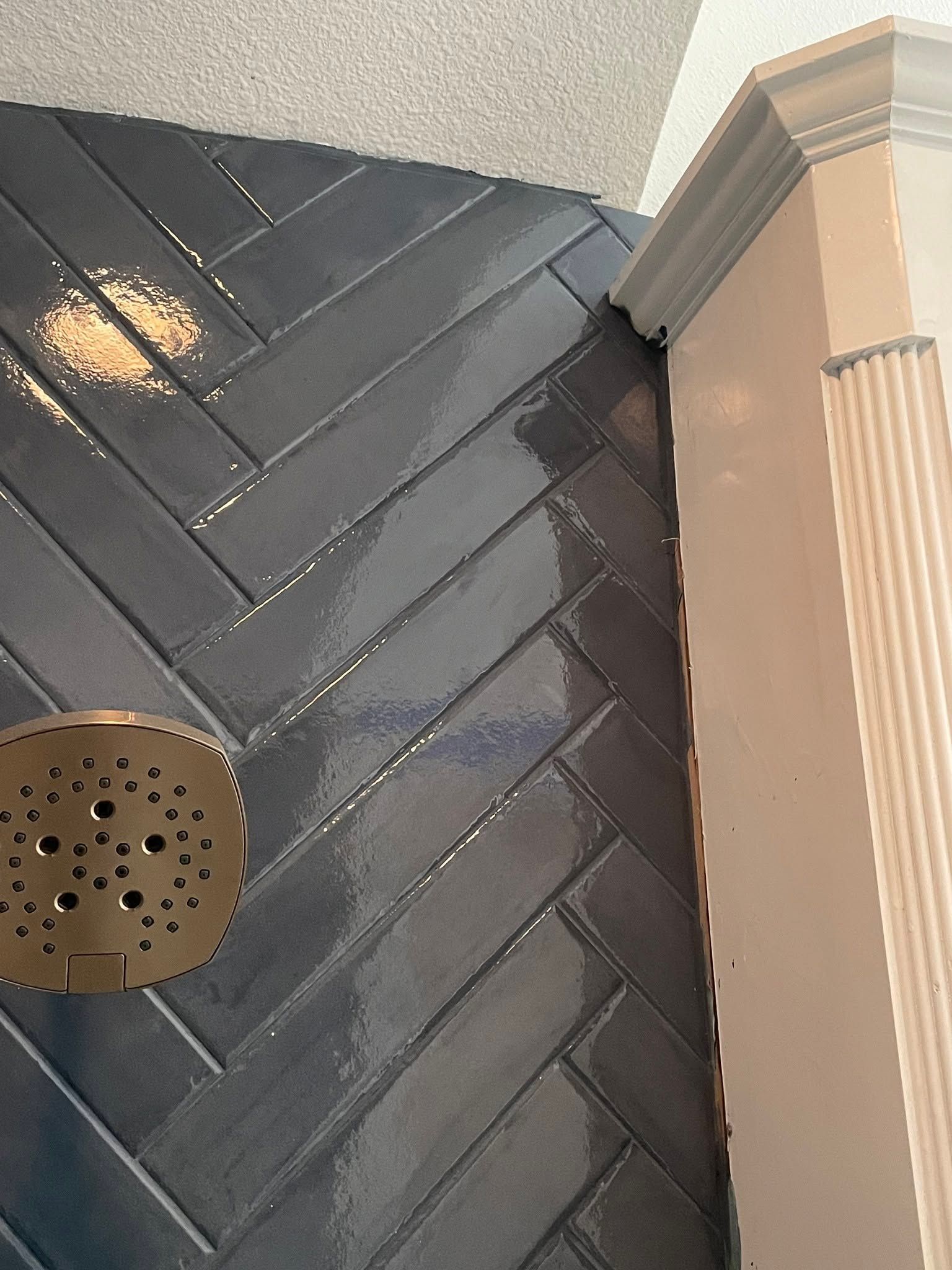 Black herringbone tile floor beside a beige wall and shower drain