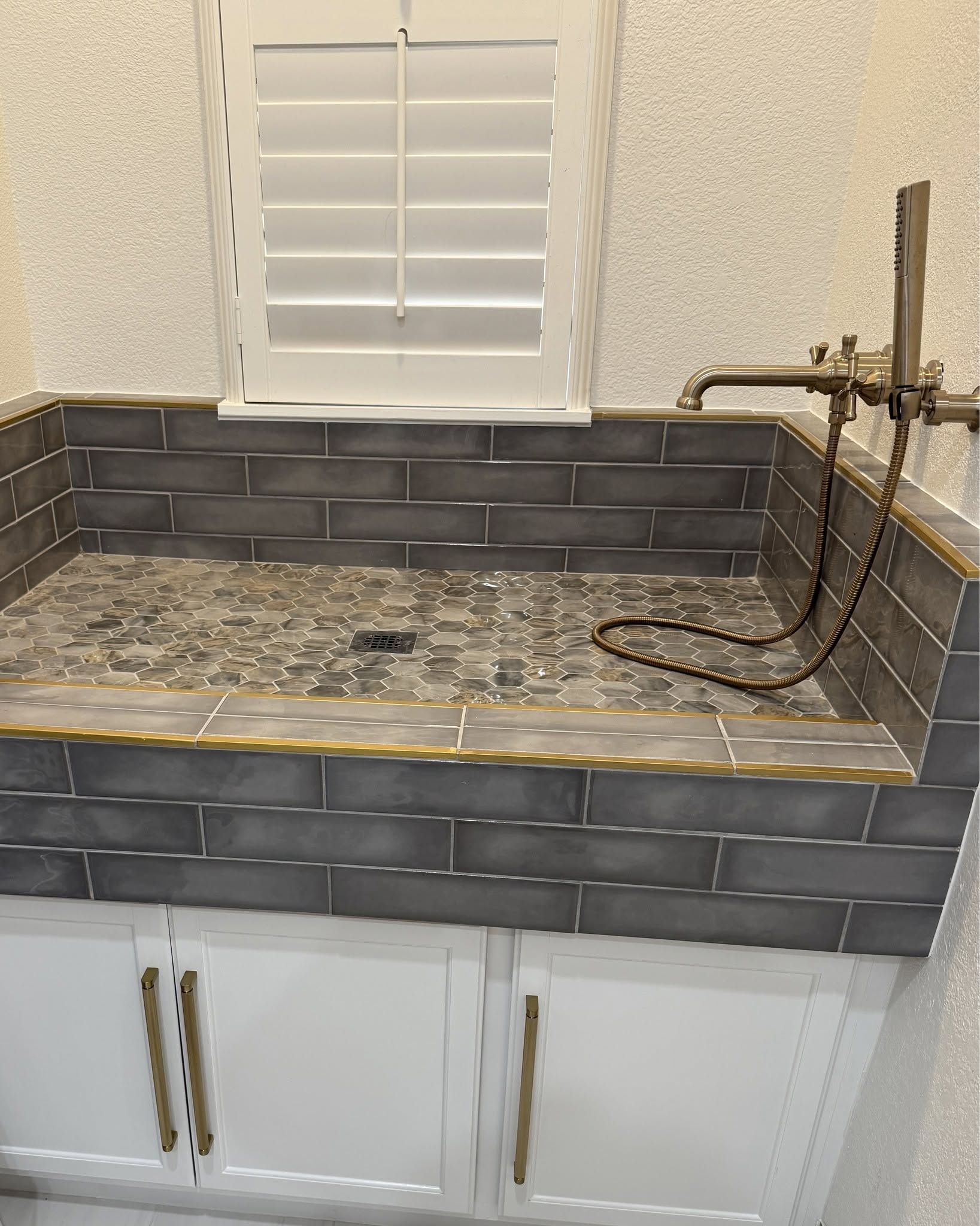 Modern bathroom vanity with gray mosaic countertop, dark tile backsplash, and window above sink area