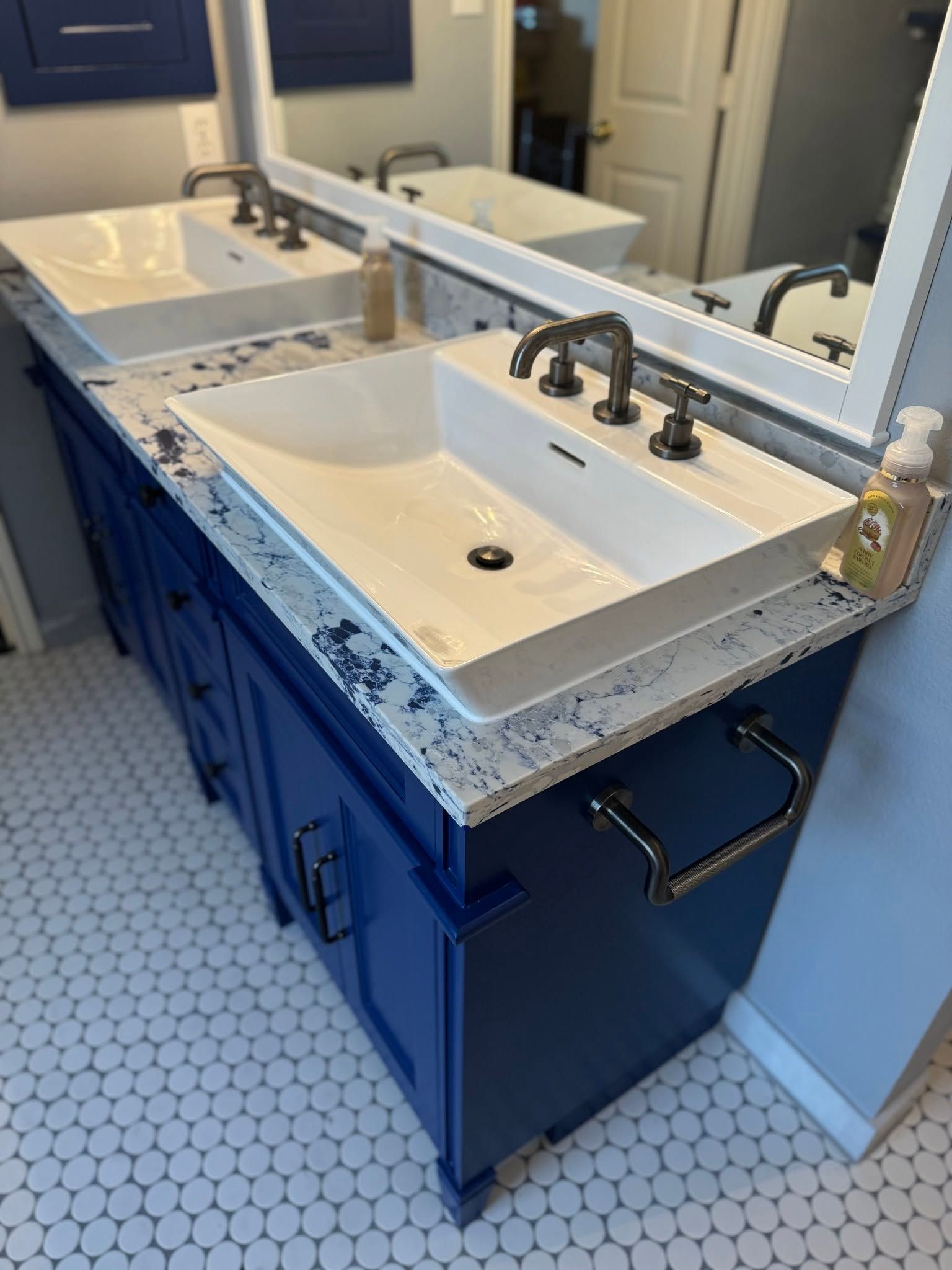 Bathroom double vanity with white sinks, chrome faucets, blue cabinets, and speckled gray countertop.