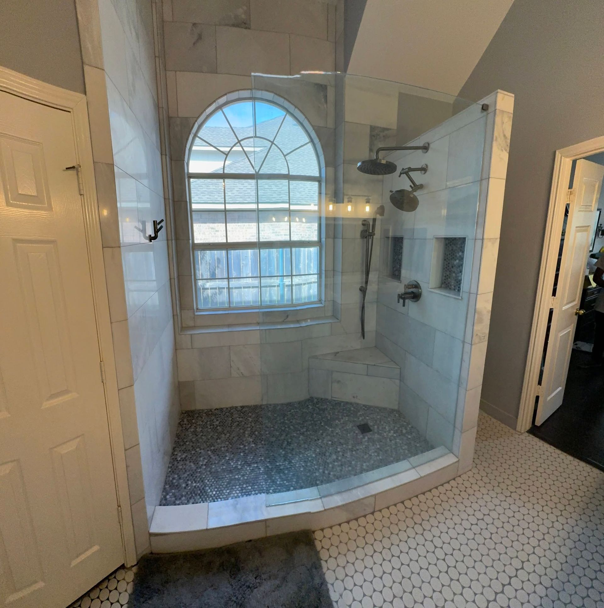 Empty tiled shower with glass door and arched window in a bright bathroom