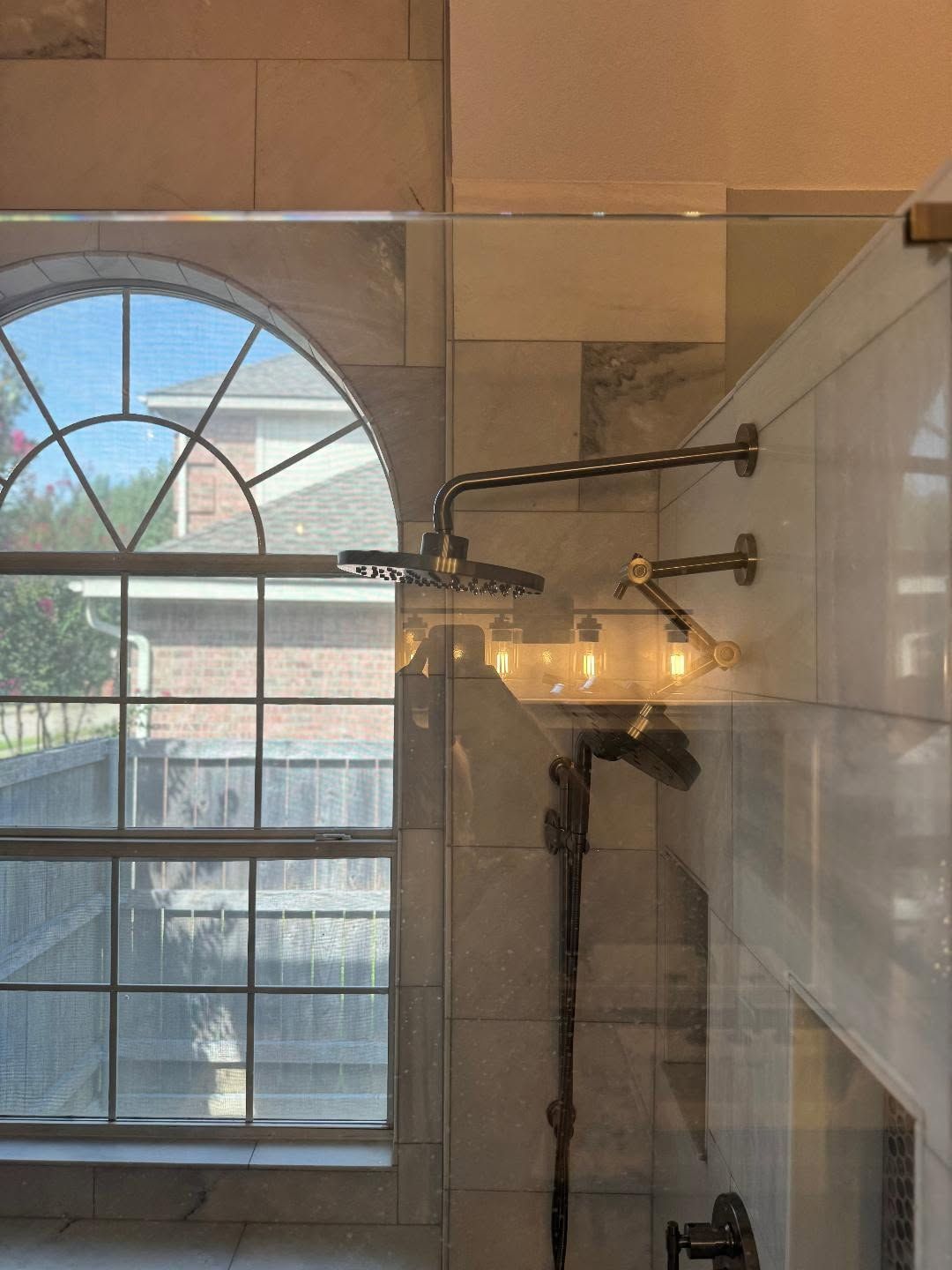 Bathroom with glass shower, arched window, and wall-mounted light fixtures