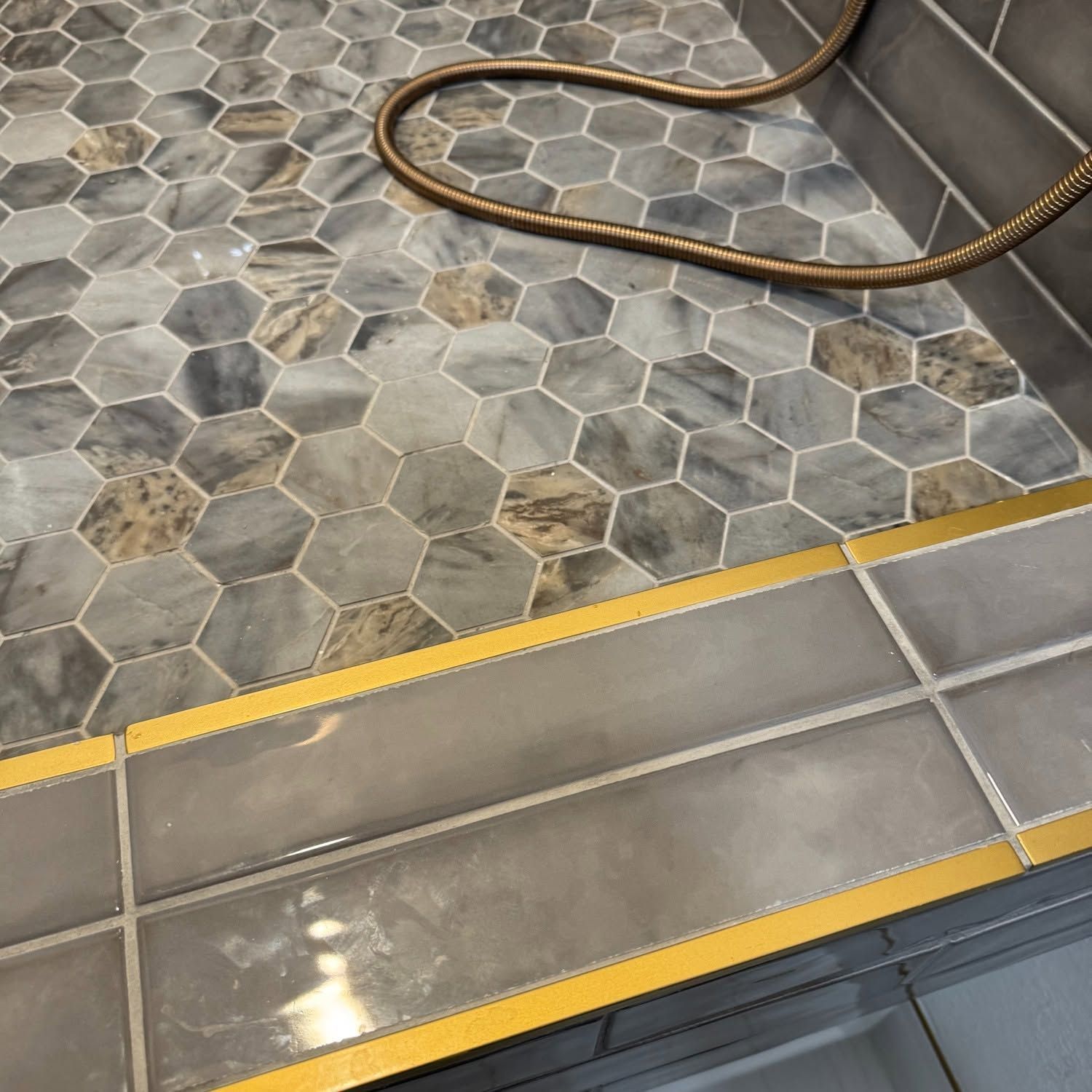 Coiled hose on gray hexagonal patio tiles beside a yellow safety strip and concrete step edge