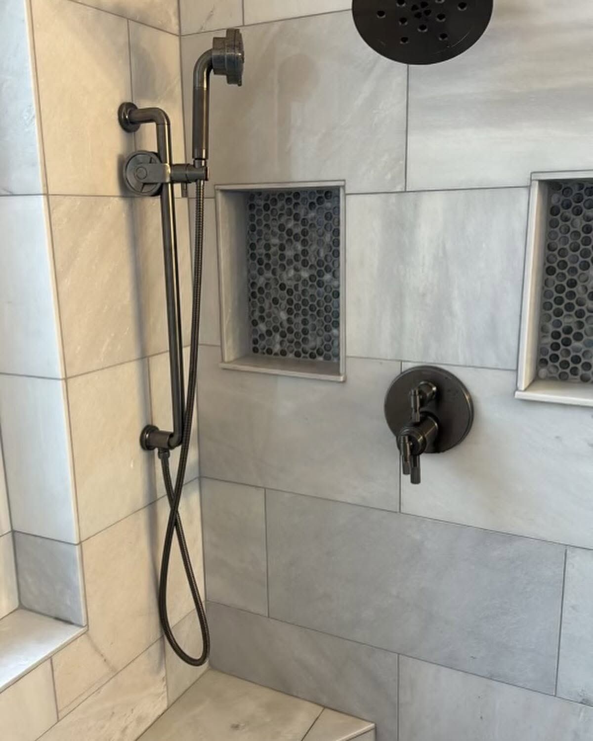 Modern shower with black fixtures, handheld sprayer, tiled walls, and two recessed mosaic shelves.