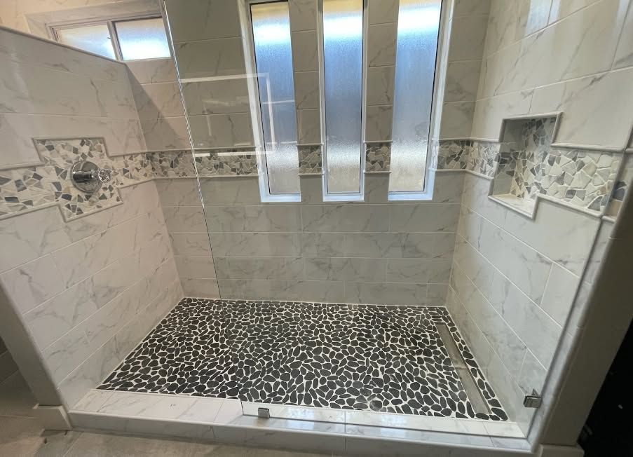 Modern tiled shower with pebble floor, glass door, and small mosaic accent tiles
