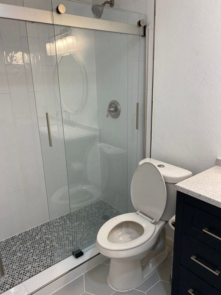 Bathroom with a glass-enclosed shower, tiled floor, and an open toilet beside a dark vanity.