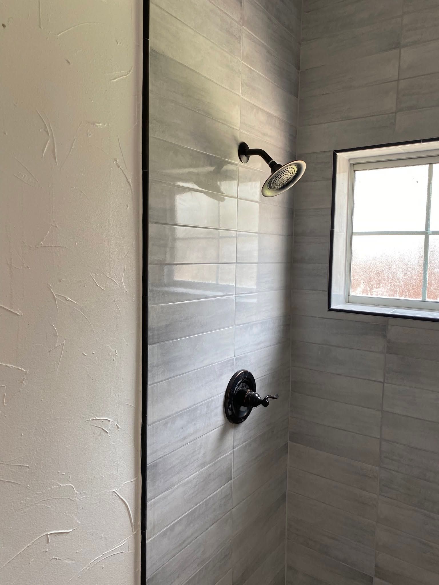 Tiled shower stall with two showerheads and a window letting in daylight