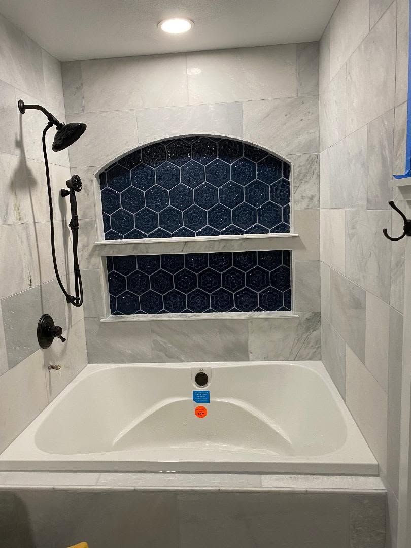 Shower and bathtub combo with gray tile and blue patterned niche shelves