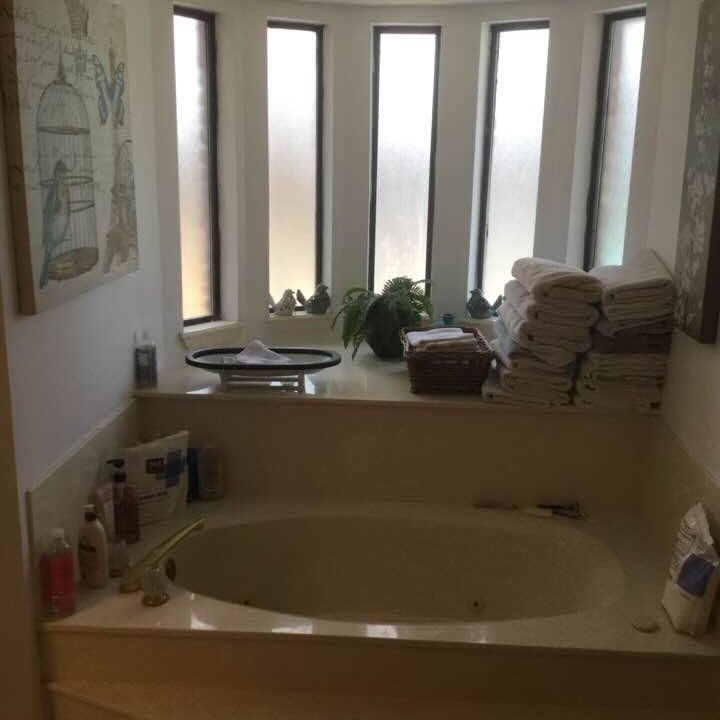 Bathroom with a bathtub, frosted windows, potted plant, and stacked towels on the ledge.
