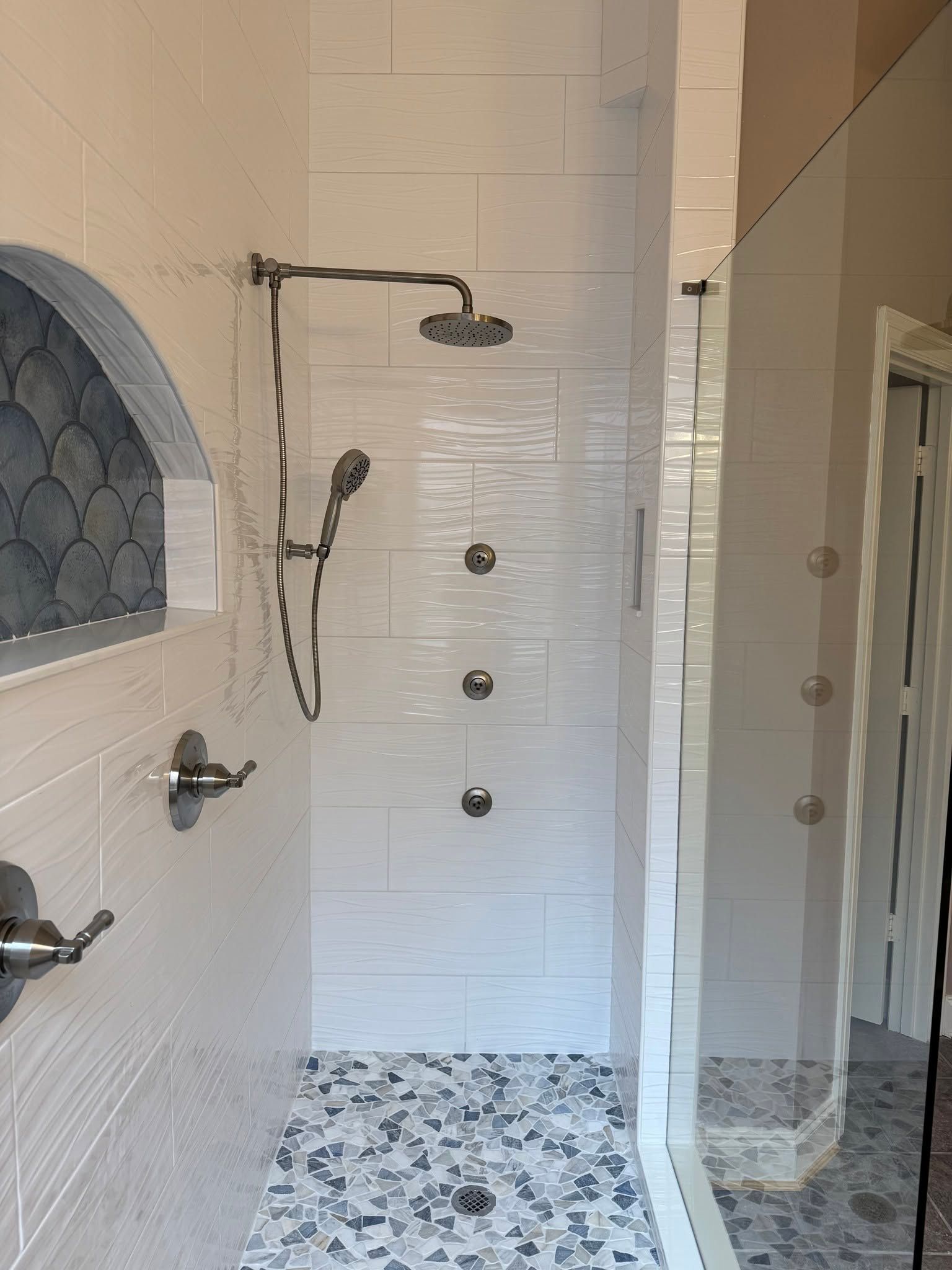 Walk-in shower with white tile, black-and-white mosaic floor, and chrome fixtures