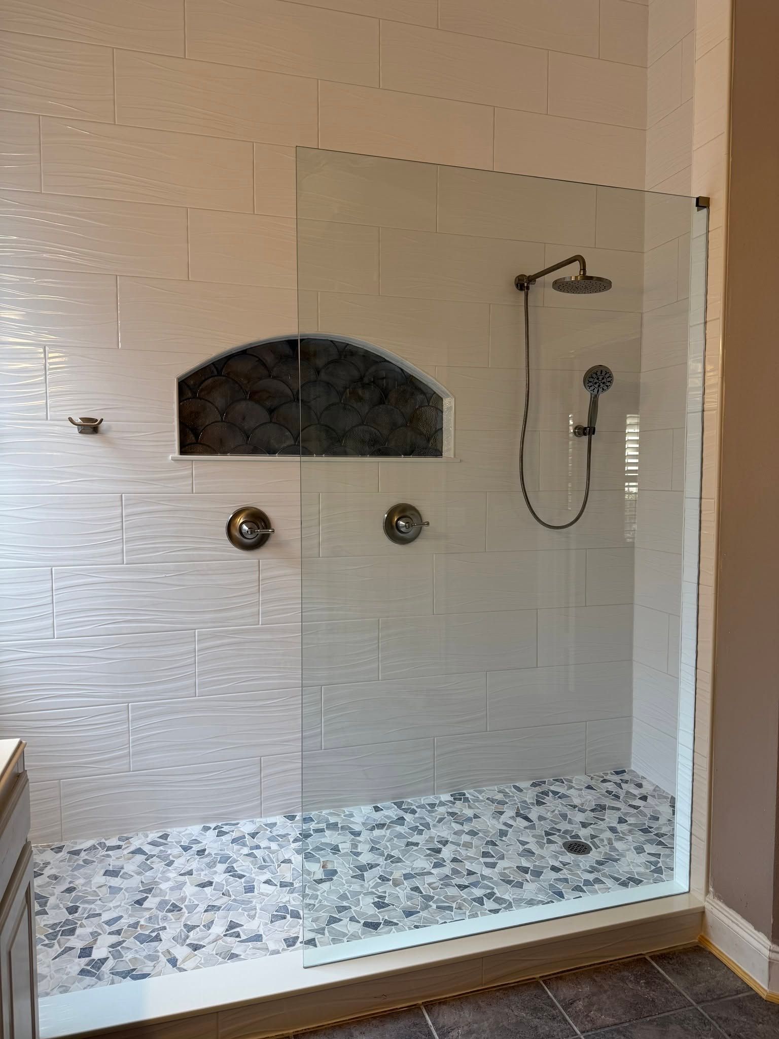 Walk-in shower with white tile walls, mosaic floor, built-in niche, and handheld showerhead