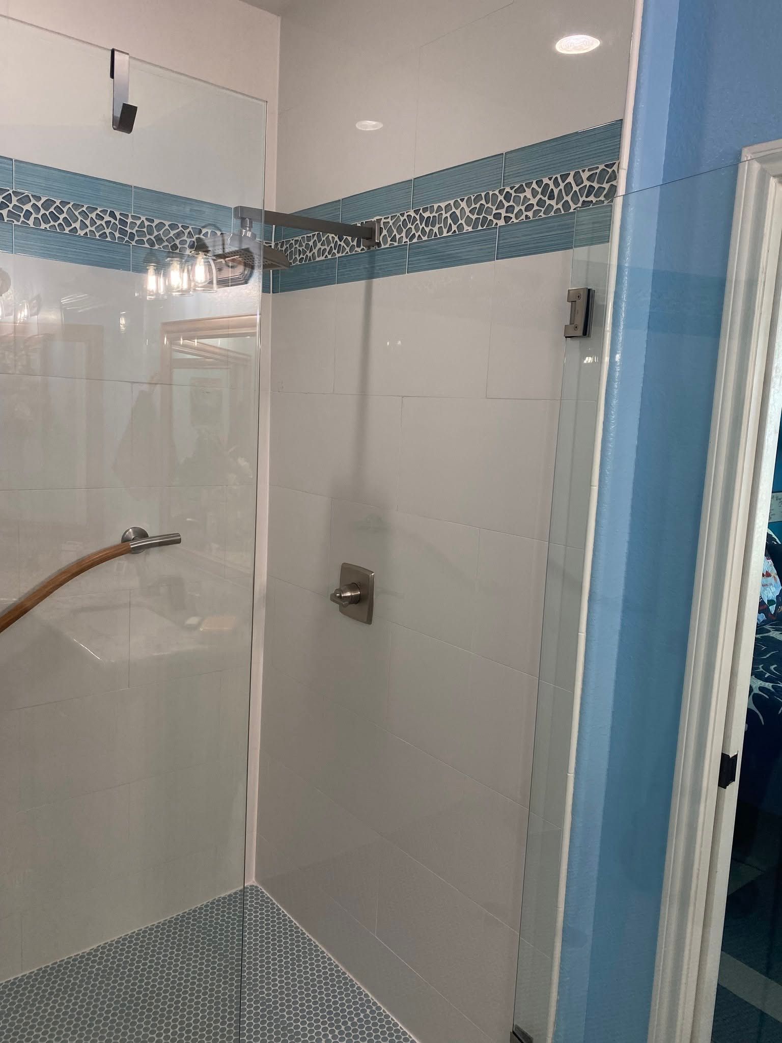 Blue-tiled glass shower enclosure in a bathroom with white walls and chrome fixtures
