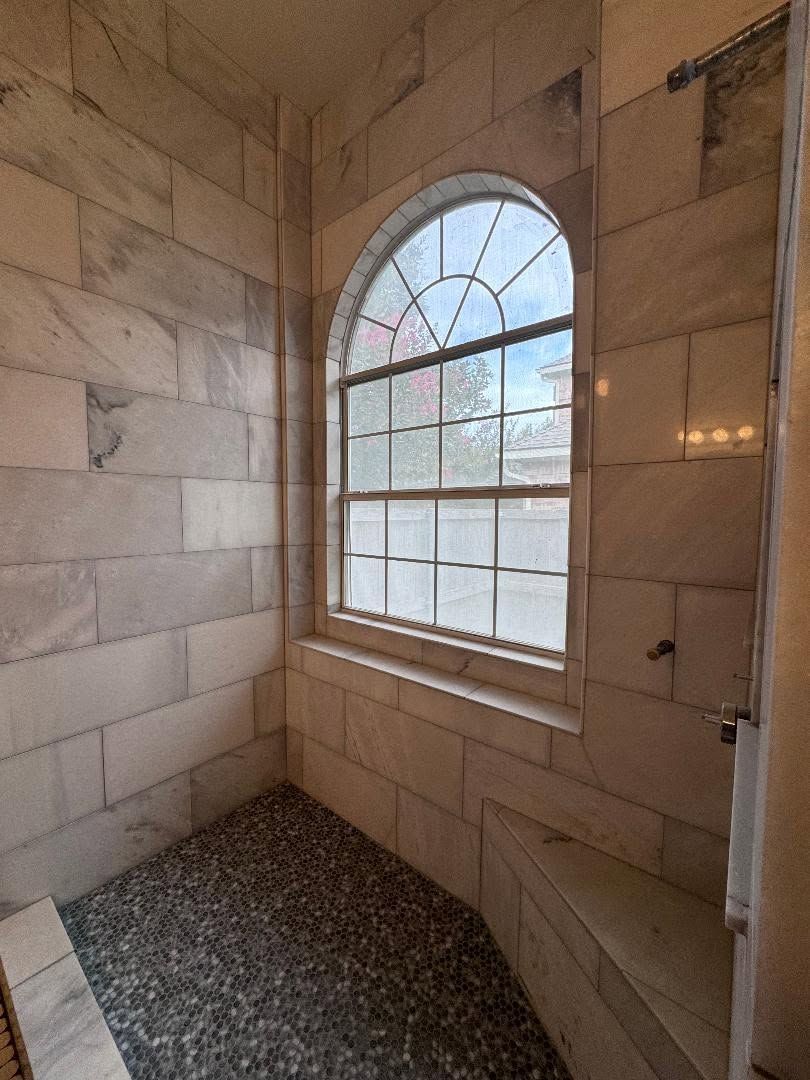 Stone-tiled shower with arched window and gravel floor, lit by natural light