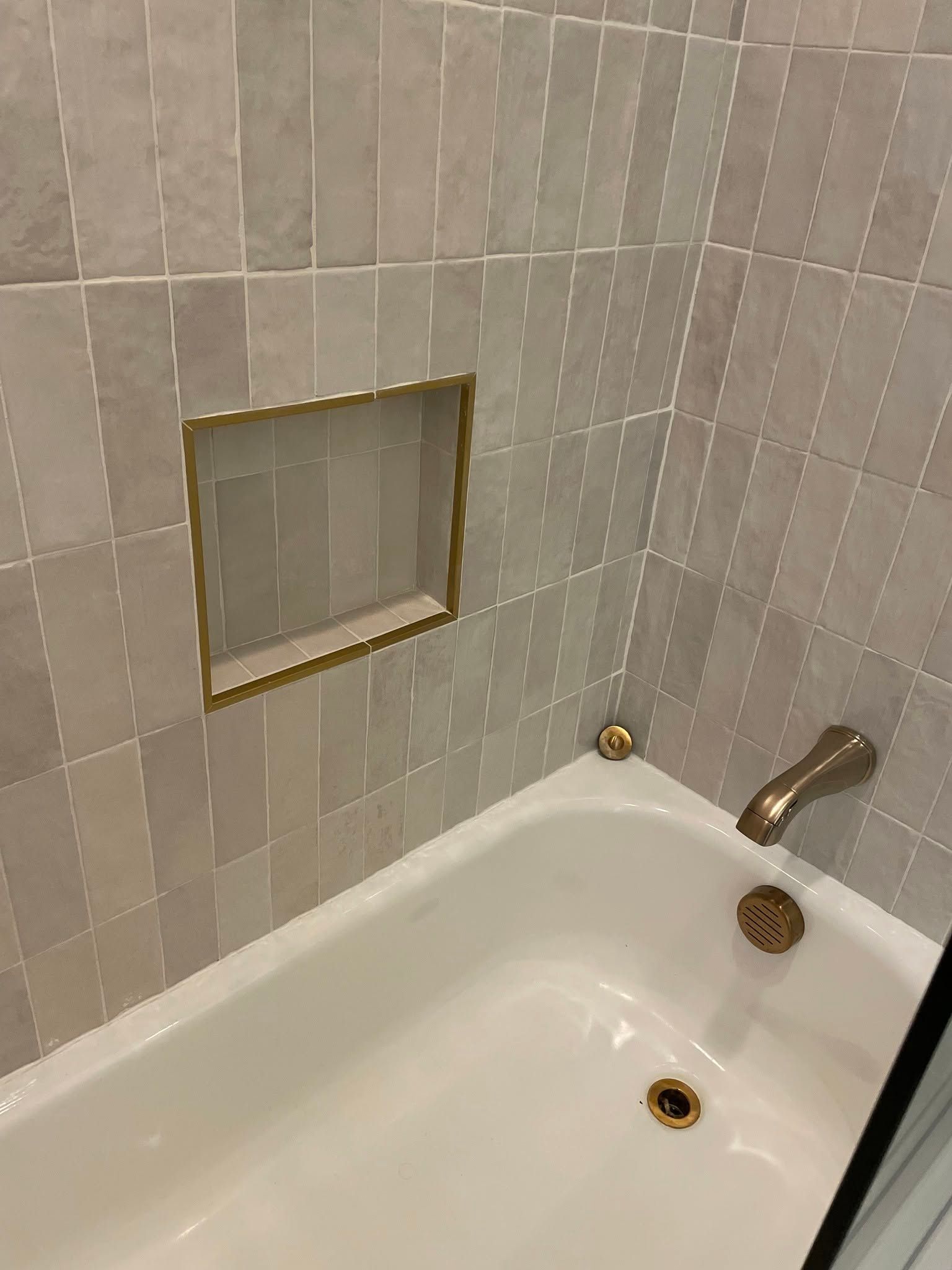 Bathtub with tiled wall and a small framed shower niche in a bathroom