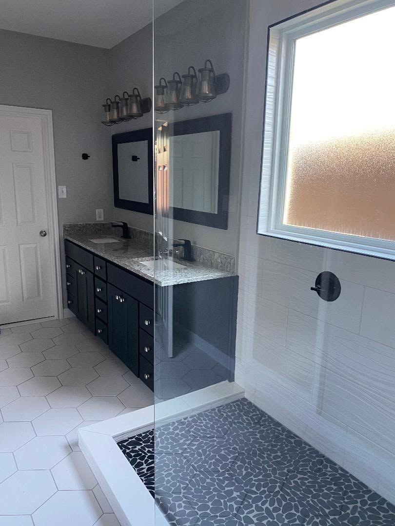 Modern bathroom with black vanity, large mirror, hex tile floor, and frosted window.