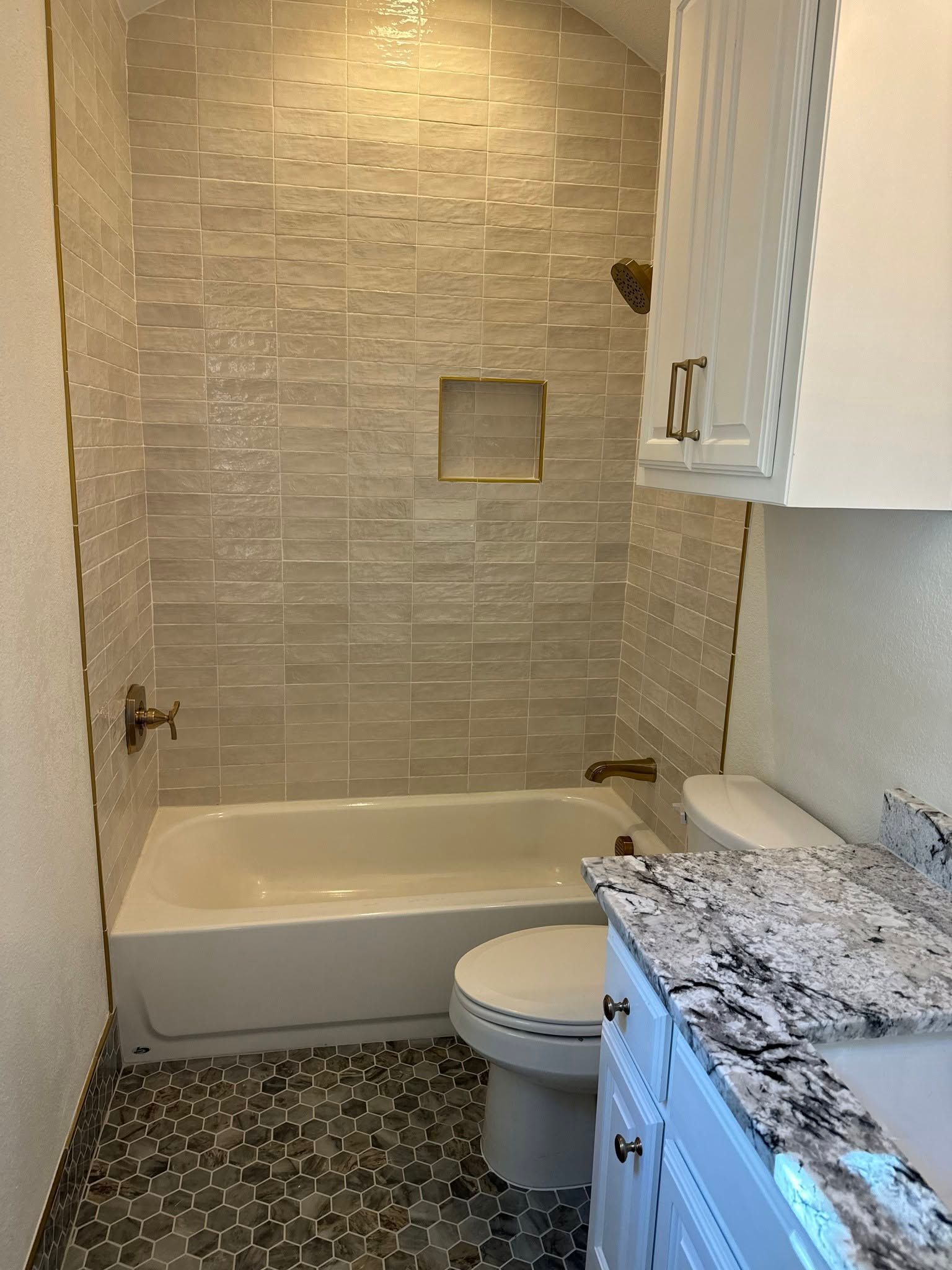 Small bathroom with tiled shower-tub, toilet, and speckled granite vanity countertop.