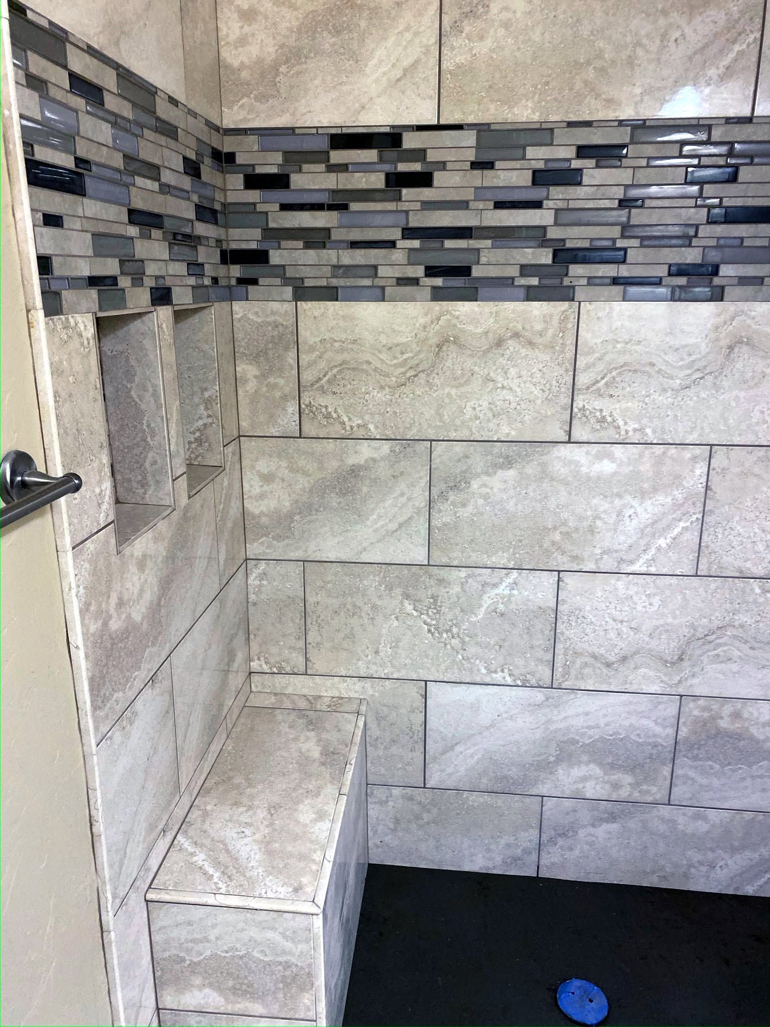 Stone-tiled shower with bench, decorative mosaic border, and dark floor drain.