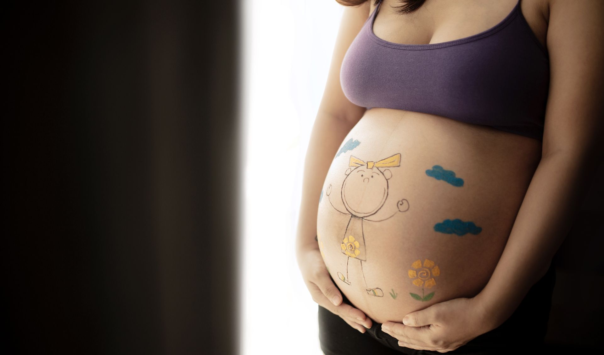 An expectant mother happily cradles her belly, showing confidence and peace after receiving holistic prenatal care.
