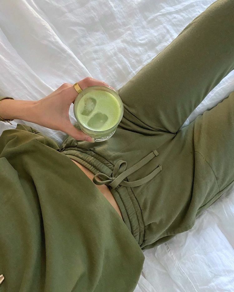 Uma mulher está deitada na cama segurando um copo de chá verde.