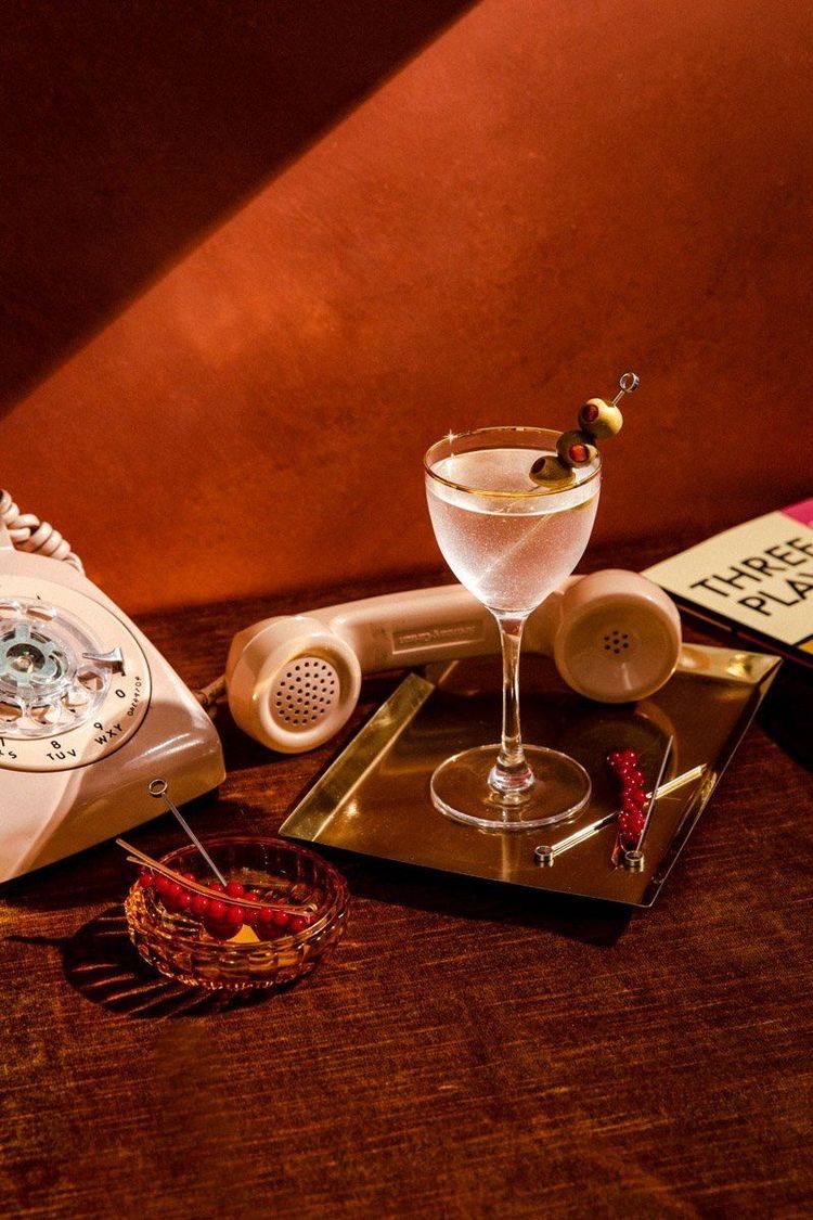 Um martini está sobre uma mesa ao lado de um telefone e um livro.