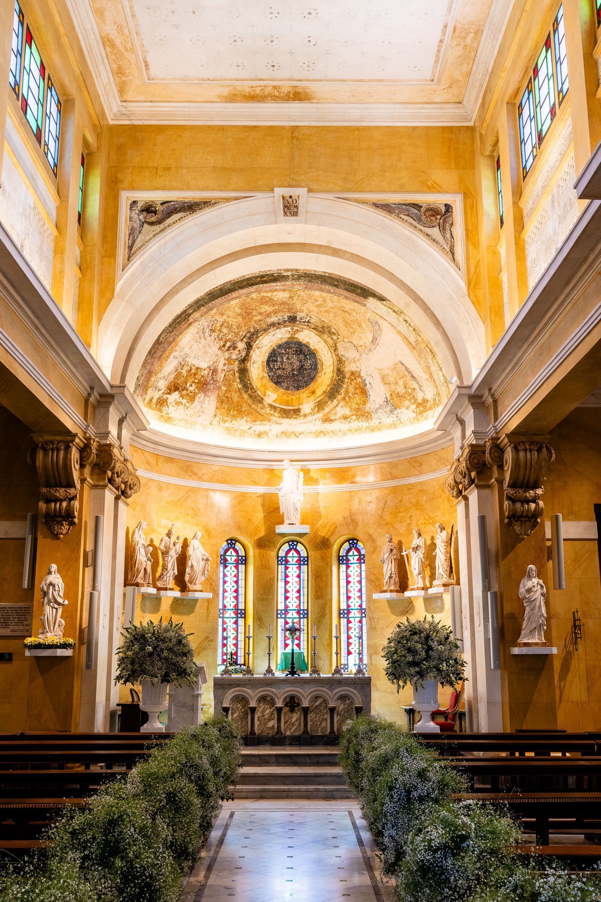 O interior de uma igreja com vitrais e flores.