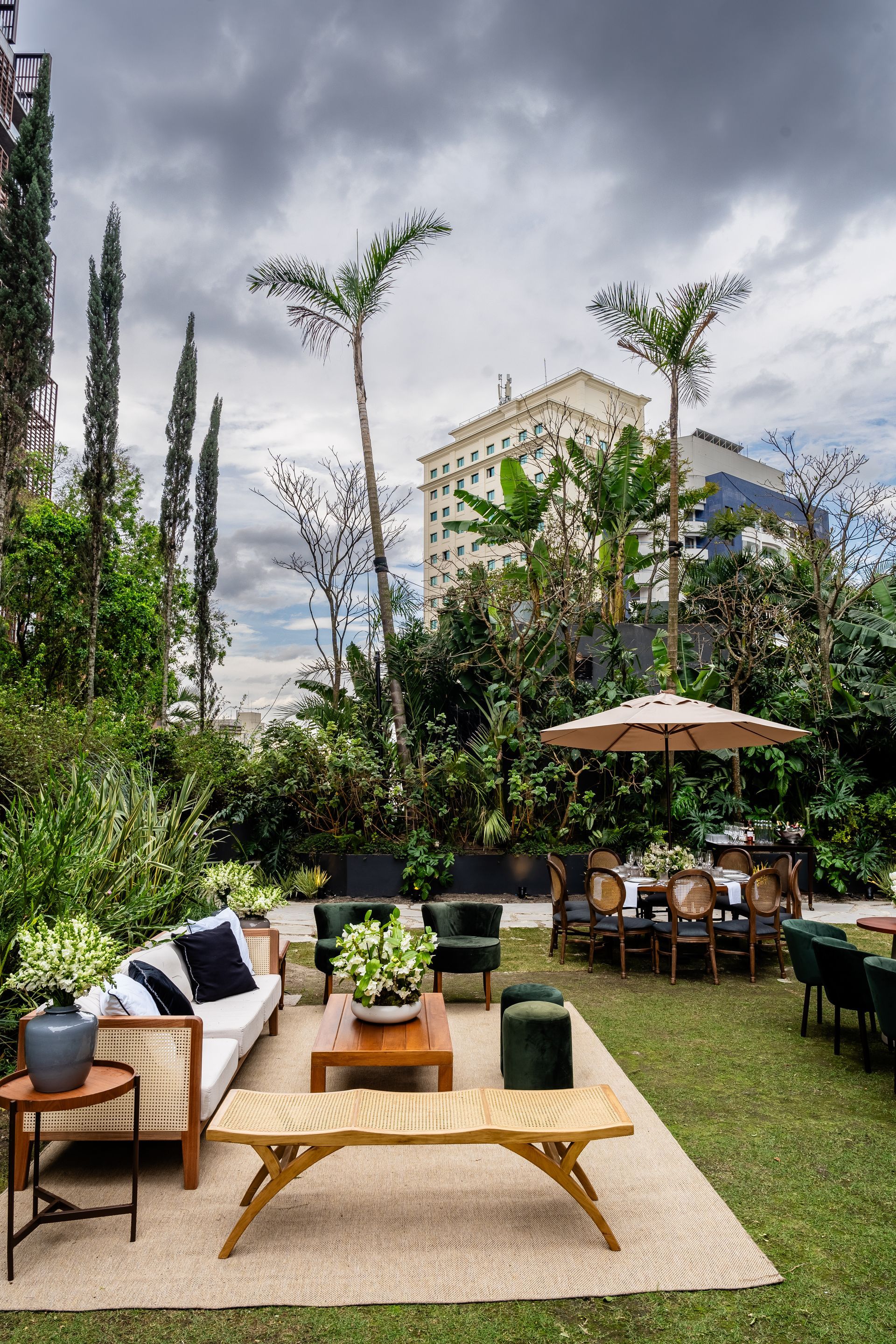 Um jardim verdejante com um sofá, mesa, cadeiras e guarda-sóis.