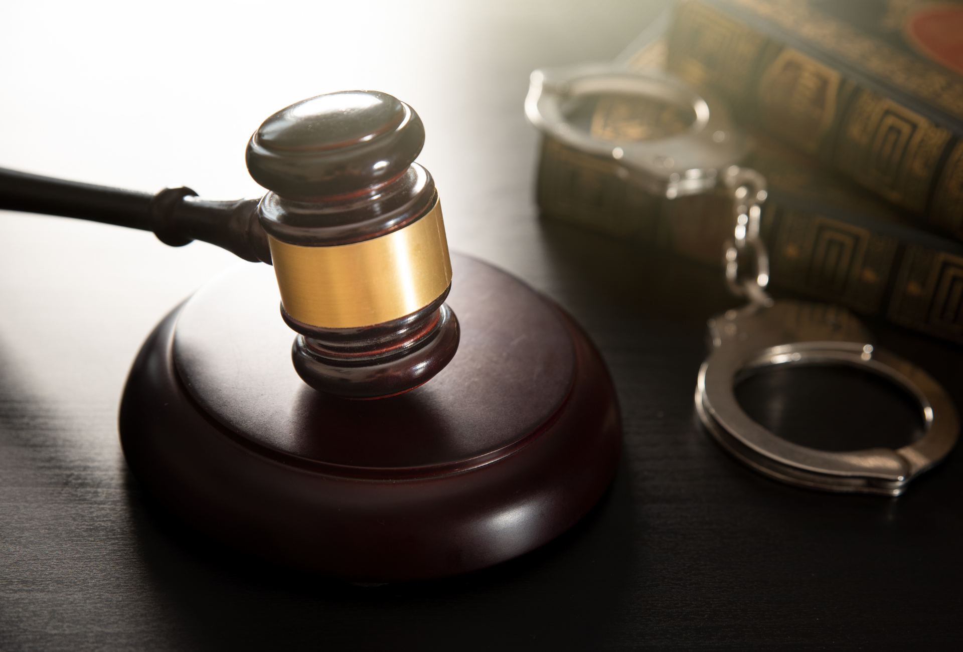 Gavel, handcuffs, and legal books on a dark surface, symbolizing law and justice.