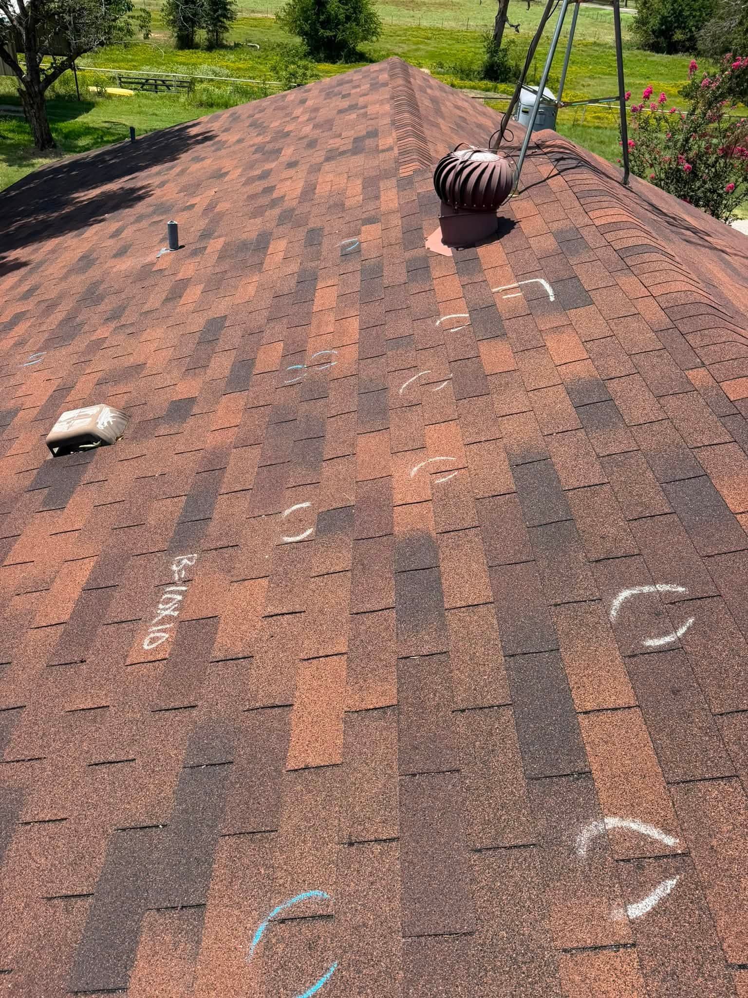 Weathered shingle roof with two vents and chalk markings, viewed from above outdoors.