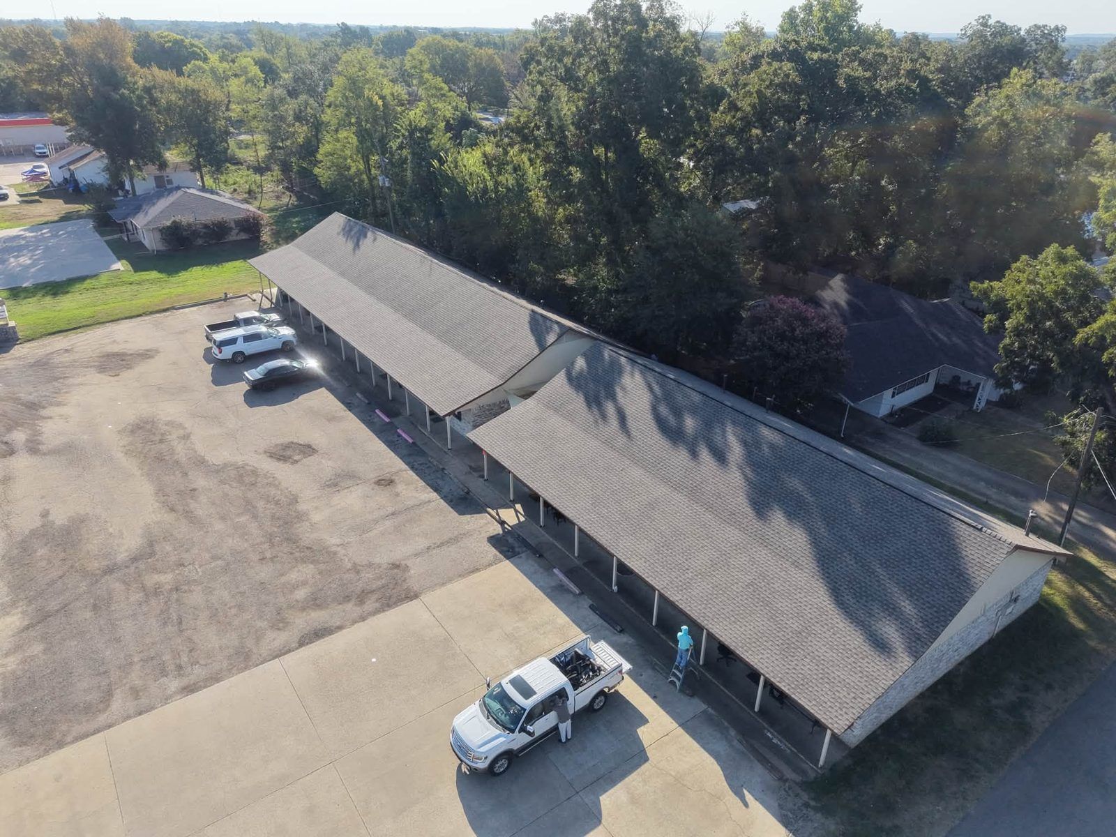 Aerial view of a long gray-roofed commercial building with several parked trucks and cars in the lot.