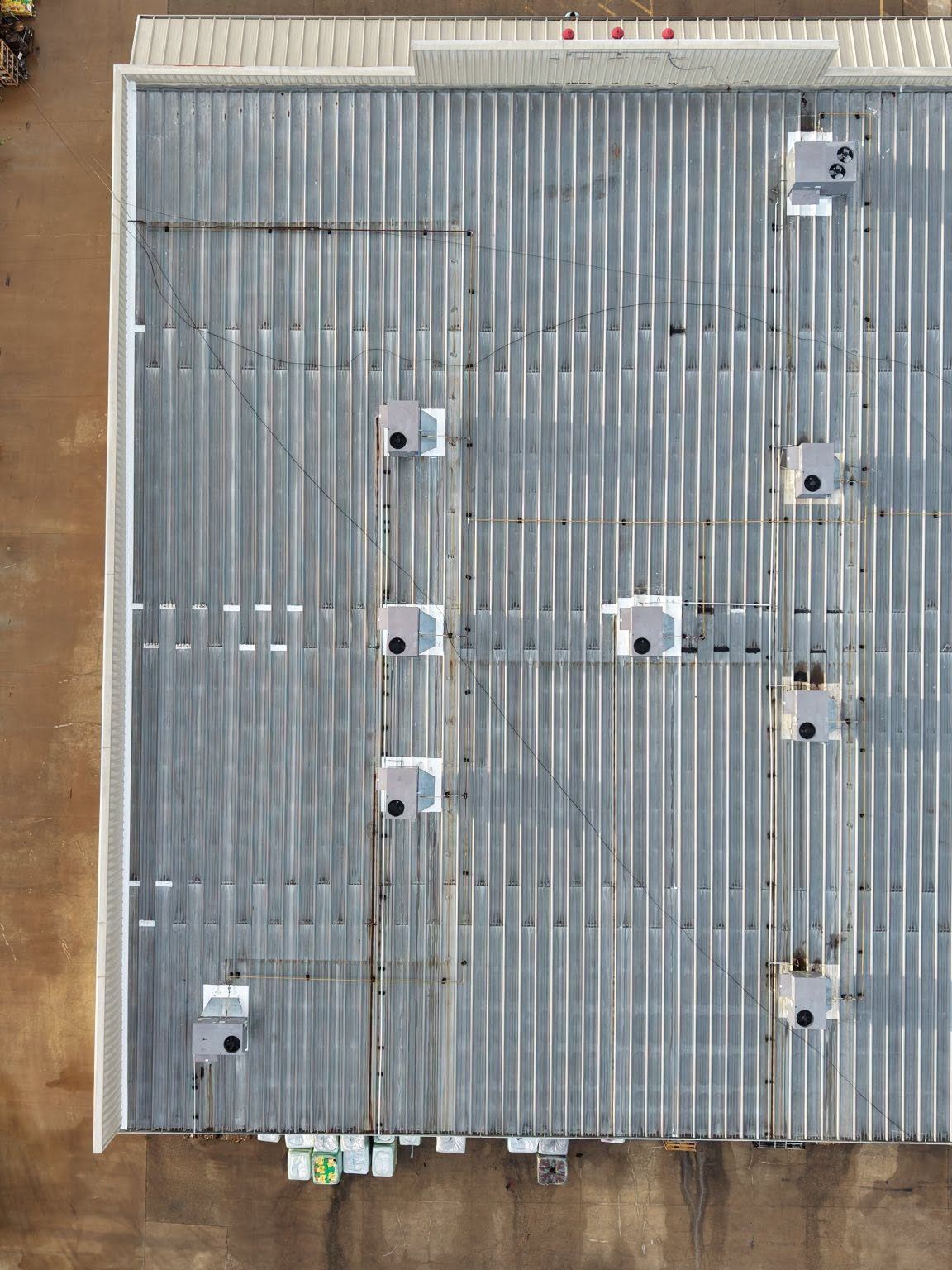 Top-down view of a corrugated metal roof with vents, pipes, and rooftop equipment.