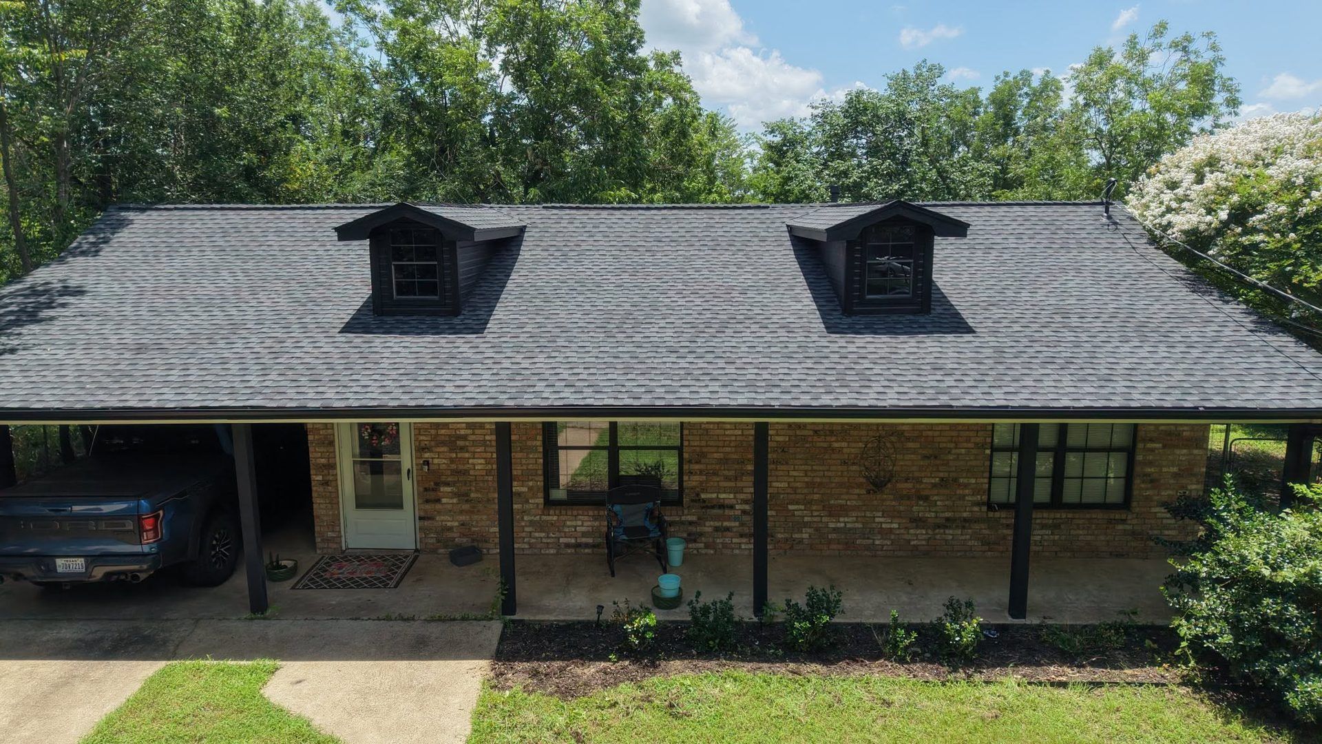 Brick house with dark gray roof, covered porch, and two dormer windows, viewed from the front.