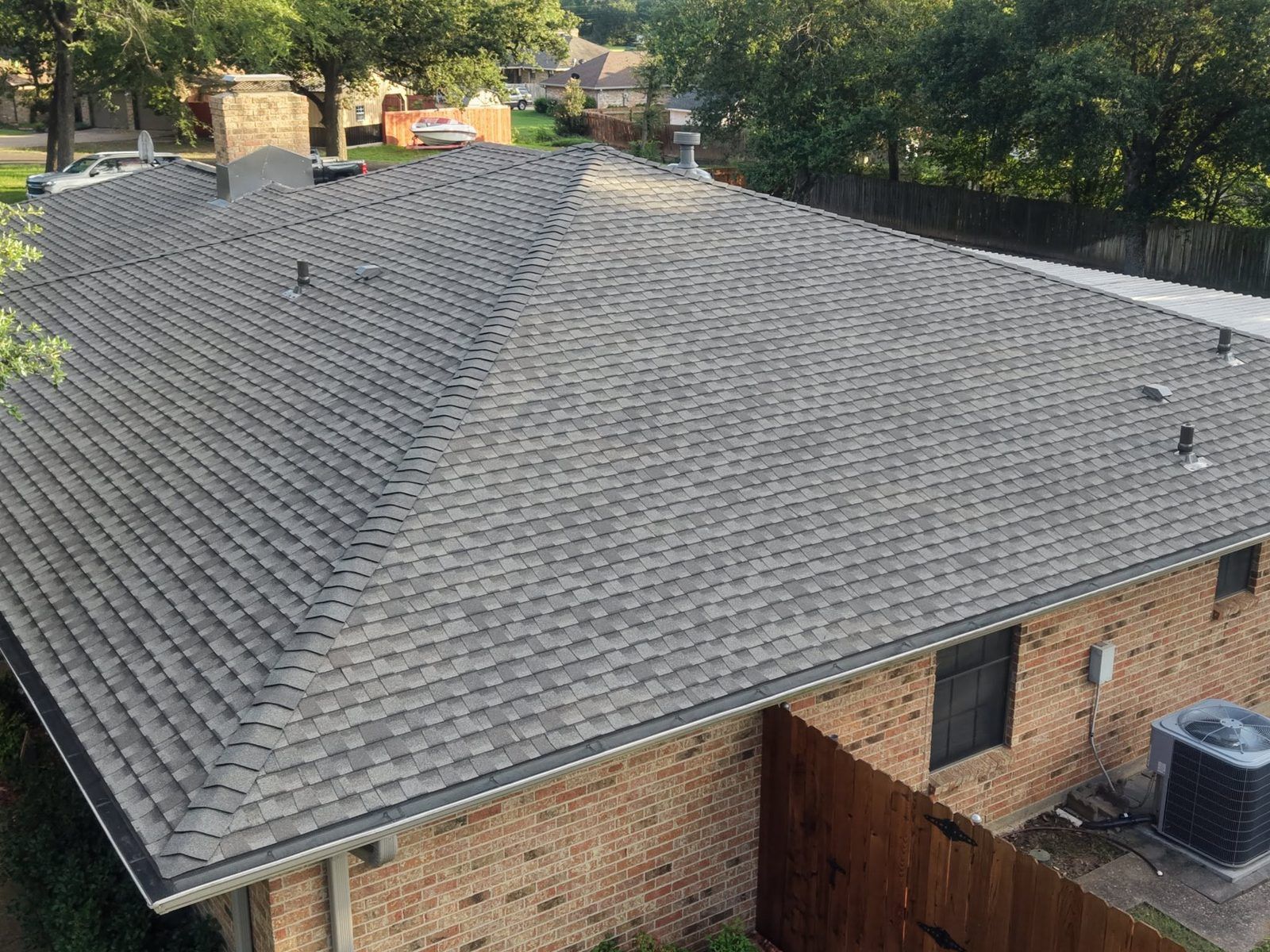 Aerial view of a brick house with a gray shingled roof and backyard trees.