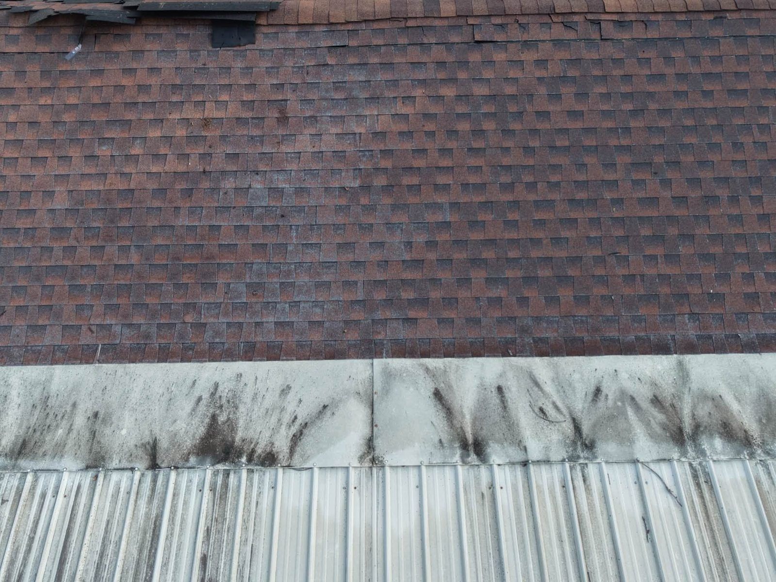 Weathered brick wall with a stained concrete ledge and corrugated metal below