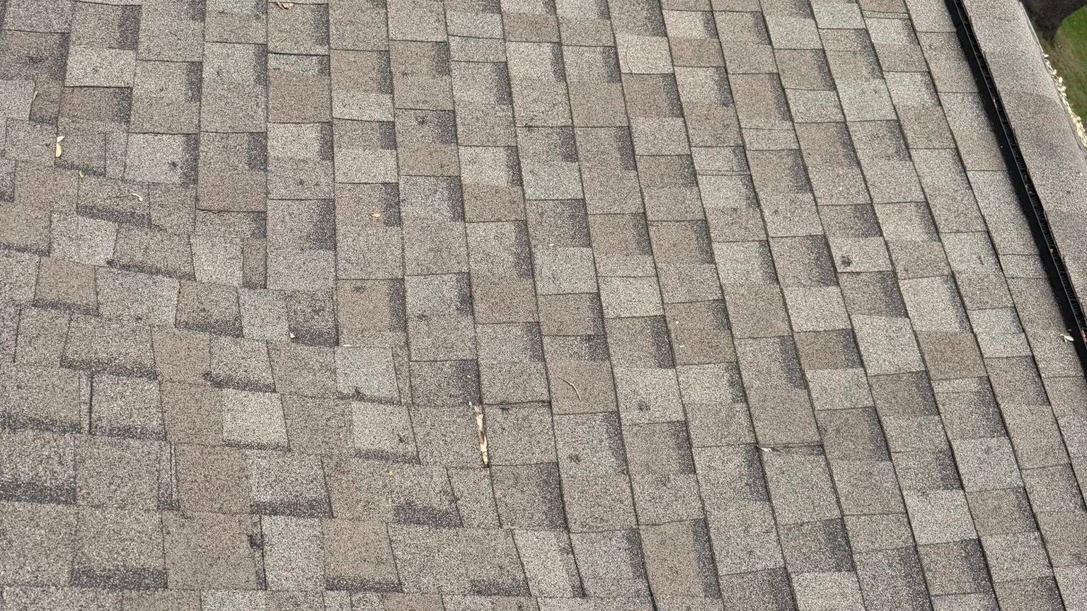 Close-up of gray asphalt shingles on a roof, with a black vent pipe at the right edge.